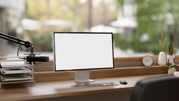 A minimalist podcast studio featuring a microphone, a computer with a white screen mockup, and decor photo