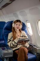 Charming Asian woman gazes at the sky view from the window while using her tablet during the flight. photo