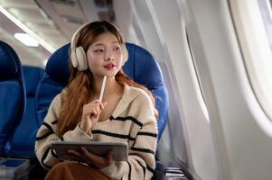 Charming Asian woman gazes at the sky view from the window while using her tablet during the flight. photo