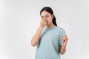 A tired, upset Asian woman taking off her glasses, suffering from eye strain, studio background. photo