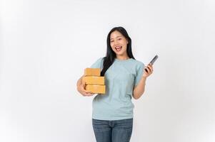 A smiling woman standing against a white studio background, holding cardboard boxes and a smartphone photo