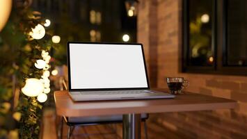 A close-up of a laptop on a table on an apartment balcony at night, illuminated by bulk lights. photo