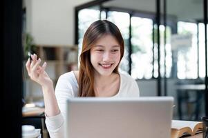 A smiling, happy Asian female college student working on her project on her laptop in a coffee shop. photo