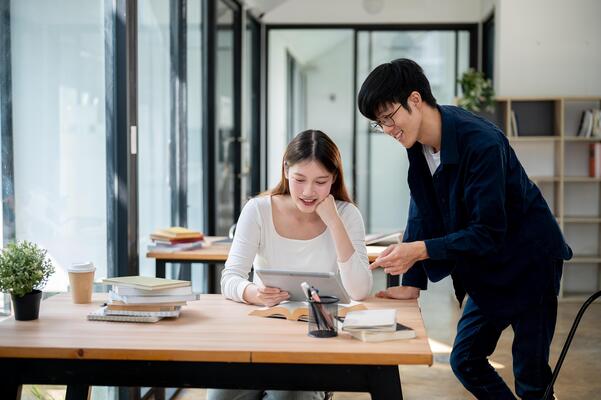 Two positive Asian college students are looking at a tablet screen and discussing.