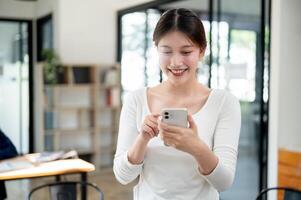 A smiling Asian female college student reading texts on her smartphone while standing in a library. photo