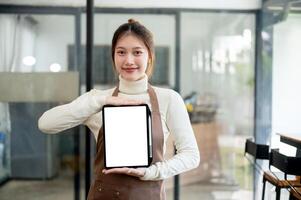 A beautiful Asian female coffee shop barista is showing a digital tablet screen to the camera. photo