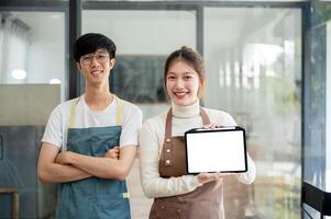 Two smiling coffee shop baristas or staff members are showing a digital tablet to the camera. photo