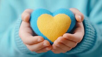 Child holding a heart with both hands, close-up. The heart is split in two colors, blue on the top half and yellow photo