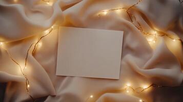 Blank card mockup lying on soft fabric, surrounded by warm fairy lights, highlighting festive atmosphere for personal messages or celebratory communication photo