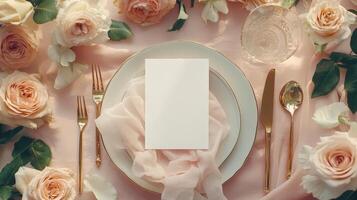 Elegant wedding table arrangement displaying blank card mock up, flat lay blush roses, golden flatware, soft pink runner highlighting romantic reception decor photo