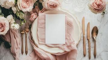 Elegant wedding table arrangement displaying blank card mock up, flat lay blush roses, golden flatware, soft pink runner highlighting romantic reception decor photo