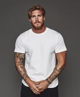 Strong man poses confidently in a plain white shirt with tattoos visible photo