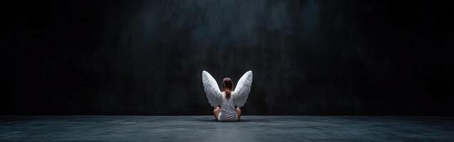 Child with angel wings sitting on a dark stage during a performance photo