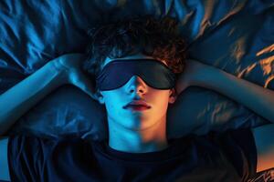 Young man resting with sleep mask on bed in dim light at night photo