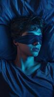 Young man resting with sleep mask while lying on blue bedding at night photo