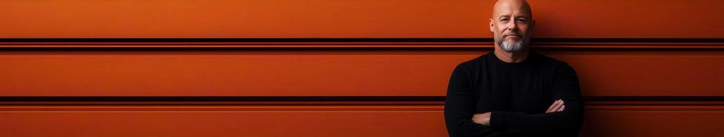 Man standing against a vibrant textured orange wall with crossed arms photo