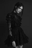 A model poses in a striking black lace dress with ruffles in a dimly lit studio photo