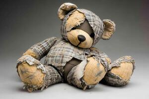 Worn teddy bear with patchy clothing sitting against a neutral background photo