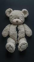 Torn teddy bear laying on a dark surface revealing stuffing inside photo