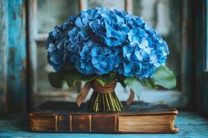 Bouquet of blue hydrangeas resting on antique book in rustic setting photo