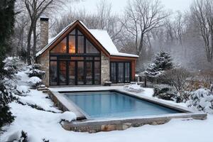 Modern pool house with illuminated interior overlooking snow covered swimming pool during winter photo