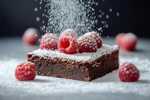 Icing sugar falling on chocolate brownie with raspberries on top photo