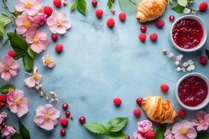 Spring breakfast with croissants, raspberry jam and flowers creating frame on blue background photo