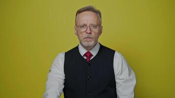 Portrait of a serious senior businessman. Mature man with grey beard in glasses standing on a yellow background and looking at camera. video