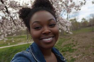 A young black woman smiling in front of a flowering tree photo