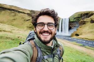 Man with glasses taking selfie in front of waterfall photo