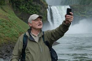 A man taking a selfie with his phone in front of a waterfall photo