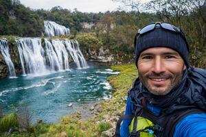 Man taking selfie in front of waterfall photo