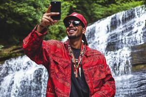 A man in a red jacket taking a selfie in front of a waterfall photo