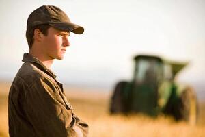A man in a hat stands in front of a tractor photo