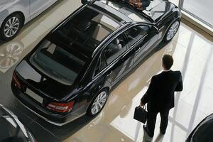 A man in a suit is looking at a car in a showroom photo