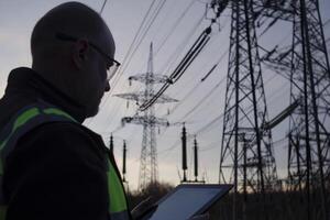 A man in a safety vest is holding a tablet computer in front of power lines photo