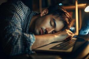 A man sleeping on a laptop in front of a lamp photo