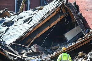 A man stands in front of a building that has been destroyed photo