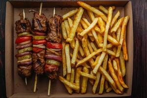A box with fries and meat skewers on a wooden table photo