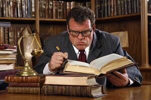 A man in a suit and tie sitting at a desk with a book and a scale photo