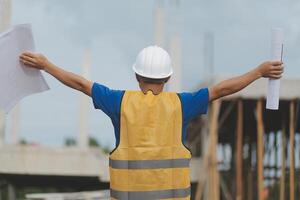 Asian man architect holds blueprint with skyscraper background, Asian male architect builder engineer design working planning confident outdoors in construction site. photo