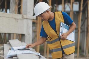 Young handsome asian civil engineer holding tablet looking forward and thinking, planning on construction building background. Evolution construction concept. photo