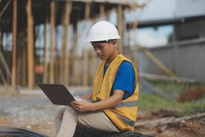 Asian man architect holds blueprint with skyscraper background, Asian male architect builder engineer design working planning confident outdoors in construction site. photo