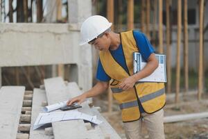Young handsome asian civil engineer holding tablet looking forward and thinking, planning on construction building background. Evolution construction concept. photo