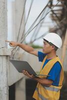 Young handsome asian civil engineer holding tablet looking forward and thinking, planning on construction building background. Evolution construction concept. photo
