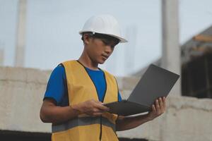 Young handsome asian civil engineer holding tablet looking forward and thinking, planning on construction building background. Evolution construction concept. photo