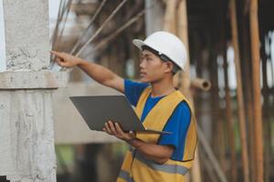 Young handsome asian civil engineer holding tablet looking forward and thinking, planning on construction building background. Evolution construction concept. photo