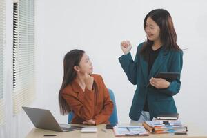 Two young Asian businesswoman discuss investment project working and planning strategy. Business people talking together with laptop computer at office. photo