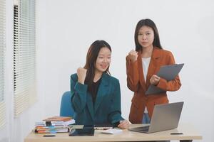 Two young Asian businesswoman discuss investment project working and planning strategy. Business people talking together with laptop computer at office. photo