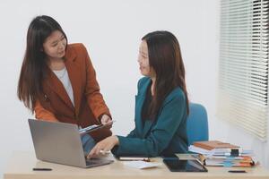 Two young Asian businesswoman discuss investment project working and planning strategy. Business people talking together with laptop computer at office. photo